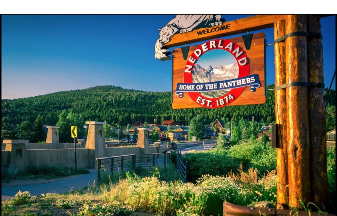 The Nederland welcome sign — &lsquo;Home of the Panthers, Est. 1874&rsquo; — above the town and the Middle Boulder Creek footbridge